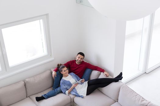 Young couple relaxing at  home using tablet computers reading in the living room on the sofa couch.