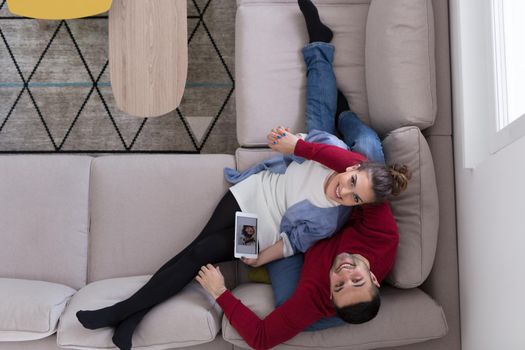 Young couple relaxing at  home using tablet computers reading in the living room on the sofa couch.