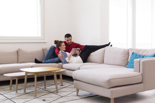 Young couple relaxing at  home using tablet computers reading in the living room on the sofa couch.