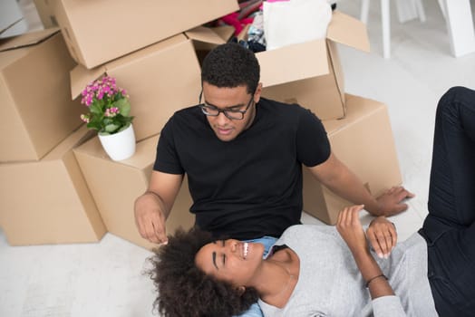 Relaxing in new house. Cheerful young African American couple sitting on the floor and drinking coffee while cardboard boxes laying all around them