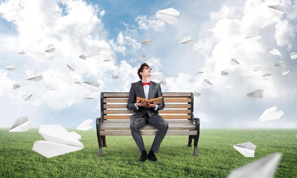 young student with a book on the bench. traditional learning concept. paper planes fly around