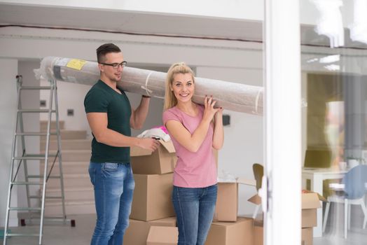 Young couple carrying a carpet moving in to new home together. Home, people, moving and real estate concept