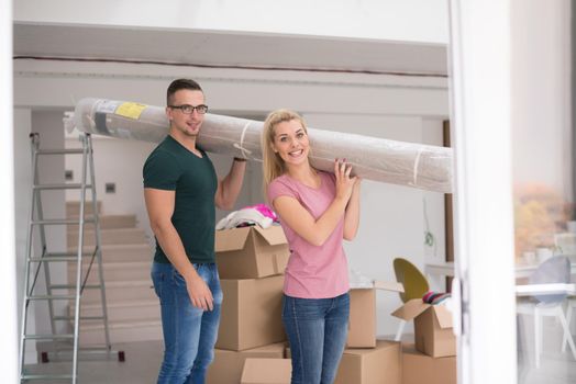 Young couple carrying a carpet moving in to new home together. Home, people, moving and real estate concept