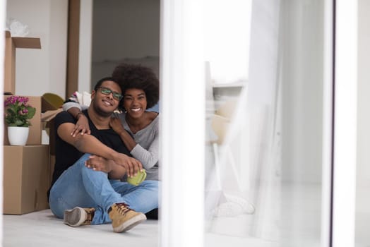 Relaxing in new house. Cheerful young African American couple sitting on the floor and drinking coffee while cardboard boxes laying all around them