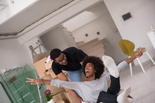 African American couple sitting in a box playing with packing material, having fun after moving in new home