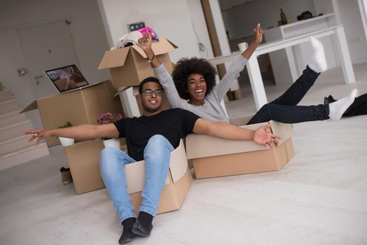 African American couple sitting in a box playing with packing material, having fun after moving in new home