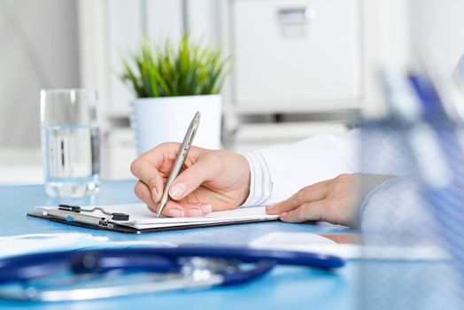 Doctor filling patient history list at clipboard. Physician in medical uniform working at desk in office. Examination and diagnosis in clinic. Doctor workplace with green plant in pot and stethoscope.