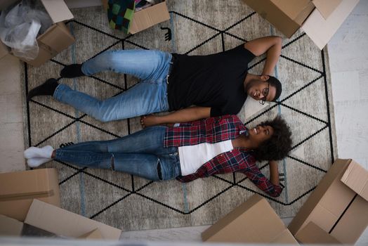 Top view of attractive young African American couple moving, holding hands, looking at camera and smiling while lying among cardboard boxes