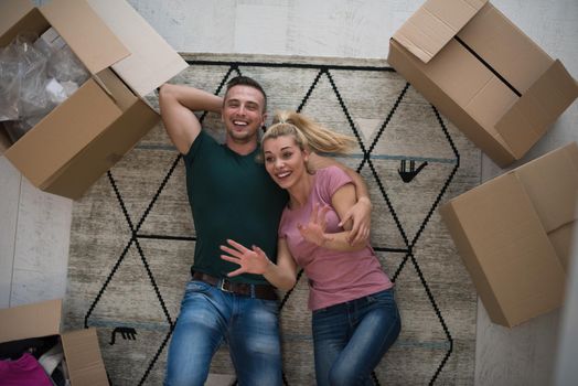 Top view of attractive young couple moving, holding hands, looking at camera and smiling while lying among cardboard boxes