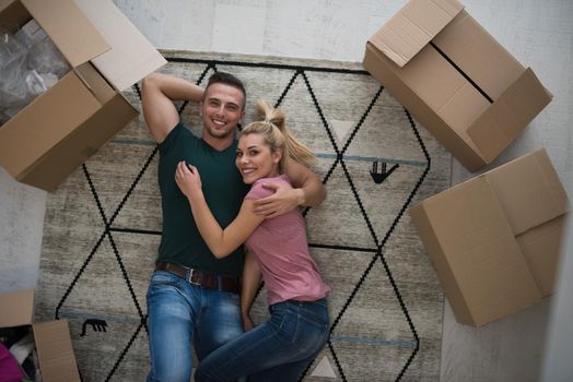 Top view of attractive young couple moving, holding hands, looking at camera and smiling while lying among cardboard boxes