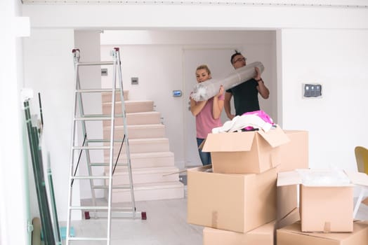 Young couple carrying a carpet moving in to new home together. Home, people, moving and real estate concept