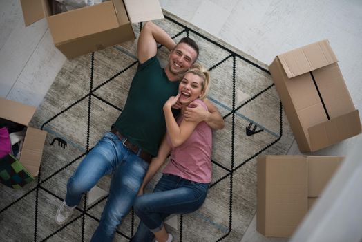 Top view of attractive young couple moving, holding hands, looking at camera and smiling while lying among cardboard boxes