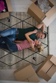 Top view of attractive young couple moving, holding hands, looking at camera and smiling while lying among cardboard boxes
