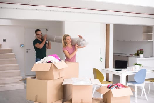 Young couple carrying a carpet moving in to new home together. Home, people, moving and real estate concept