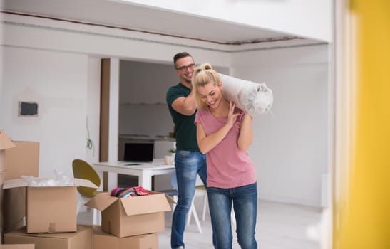 Young couple carrying a carpet moving in to new home together. Home, people, moving and real estate concept