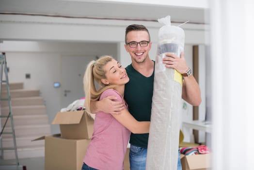 Young couple carrying a carpet moving in to new home together. Home, people, moving and real estate concept