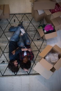 Top view of attractive young multiethnic couple moving, holding hands, looking at camera and smiling while lying among cardboard boxes