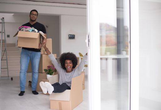 African American couple sitting in a box playing with packing material, having fun after moving in new home