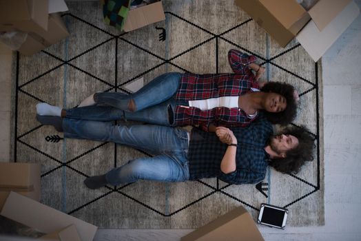 Top view of attractive young multiethnic couple moving, holding hands, looking at camera and smiling while lying among cardboard boxes