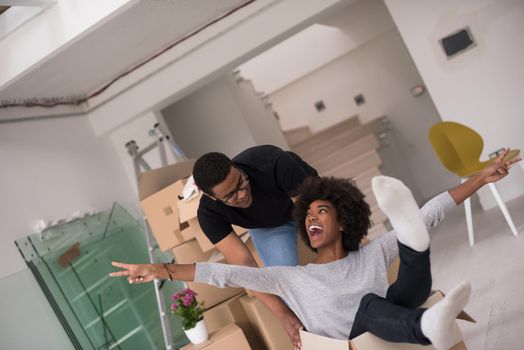 African American couple sitting in a box playing with packing material, having fun after moving in new home