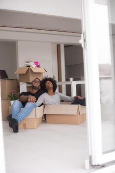 African American couple sitting in a box playing with packing material, having fun after moving in new home