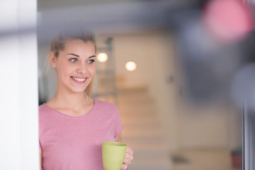 beautiful young woman drinking morning coffee by the window in her home