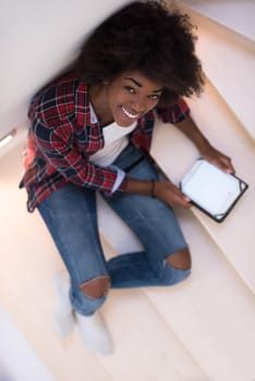 Attractive young black woman using her electronic tablet while sitting on a staircase