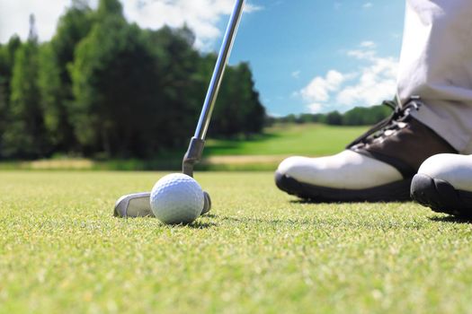 Golf player at the putting green hitting ball into a hole