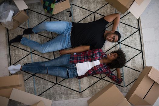 Top view of attractive young African American couple moving, holding hands, looking at camera and smiling while lying among cardboard boxes