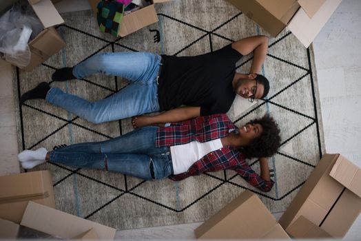 Top view of attractive young African American couple moving, holding hands, looking at camera and smiling while lying among cardboard boxes