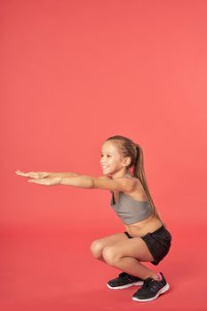 Adorable sporty girl looking away and smiling while doing exercise against red background