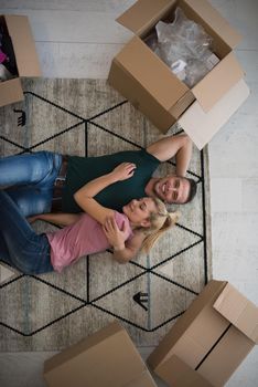 Top view of attractive young couple moving, holding hands, looking at camera and smiling while lying among cardboard boxes