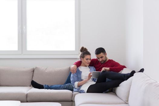 Young couple relaxing at  home using tablet computers reading in the living room on the sofa couch.