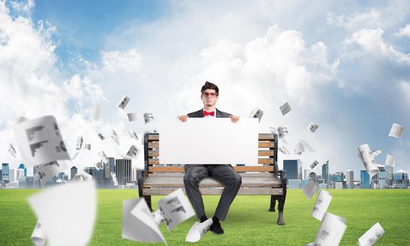 young businessman sits on a bench with an empty banner. around in the chaos flying documents