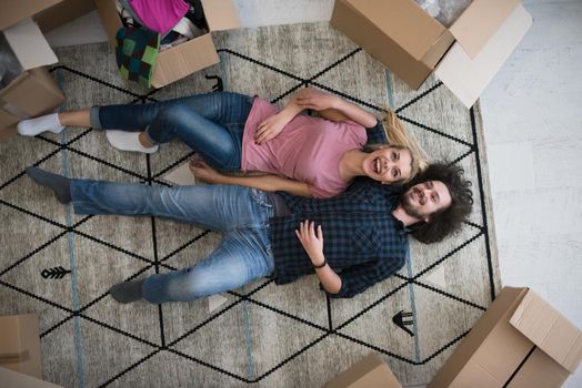 Top view of attractive young couple moving, holding hands, looking at camera and smiling while lying among cardboard boxes