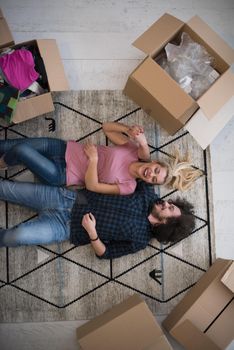 Top view of attractive young couple moving, holding hands, looking at camera and smiling while lying among cardboard boxes