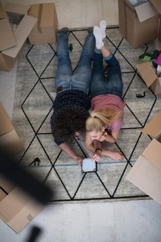 Top view of attractive young couple moving, holding hands, looking at camera and smiling while lying among cardboard boxes