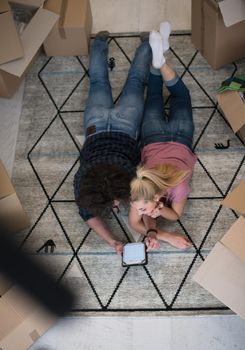 Top view of attractive young couple moving, holding hands, looking at camera and smiling while lying among cardboard boxes