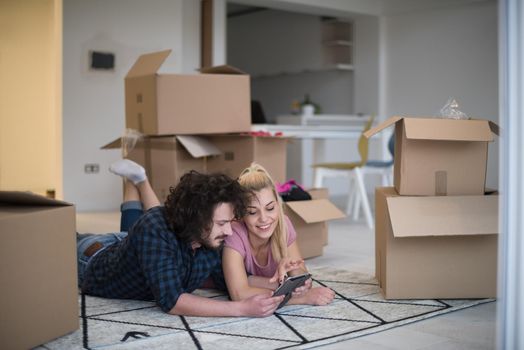 Young couple in love moving in a new flat, lying on the floor and surfing the web on a tablet computer in search of new redecoration ideas