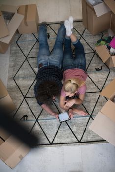 Top view of attractive young couple moving, holding hands, looking at camera and smiling while lying among cardboard boxes