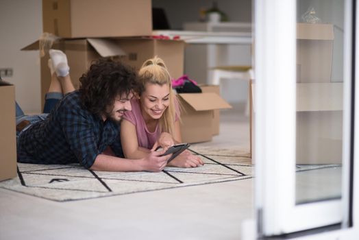 Young couple in love moving in a new flat, lying on the floor and surfing the web on a tablet computer in search of new redecoration ideas