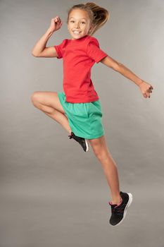 Adorable girl in shorts looking at camera and smiling while jumping in the air