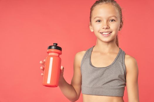 Cheerful female child with refreshing drink looking at camera and smiling while standing against red background