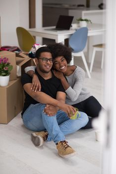 Relaxing in new house. Cheerful young African American couple sitting on the floor and drinking coffee while cardboard boxes laying all around them