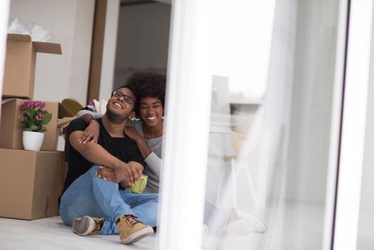 Relaxing in new house. Cheerful young African American couple sitting on the floor and drinking coffee while cardboard boxes laying all around them