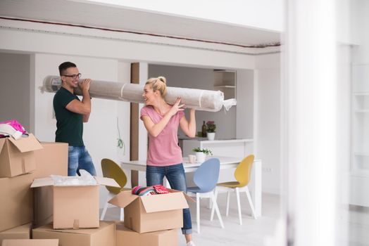 Young couple carrying a carpet moving in to new home together. Home, people, moving and real estate concept