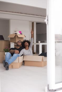 African American couple sitting in a box playing with packing material, having fun after moving in new home