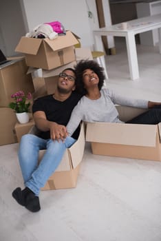 African American couple sitting in a box playing with packing material, having fun after moving in new home