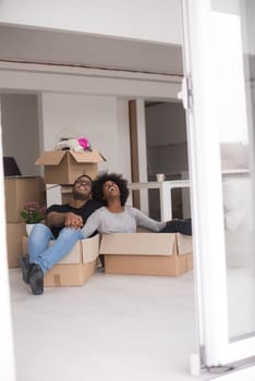 African American couple sitting in a box playing with packing material, having fun after moving in new home