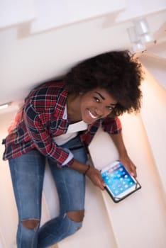 Attractive young black woman using her electronic tablet while sitting on a staircase